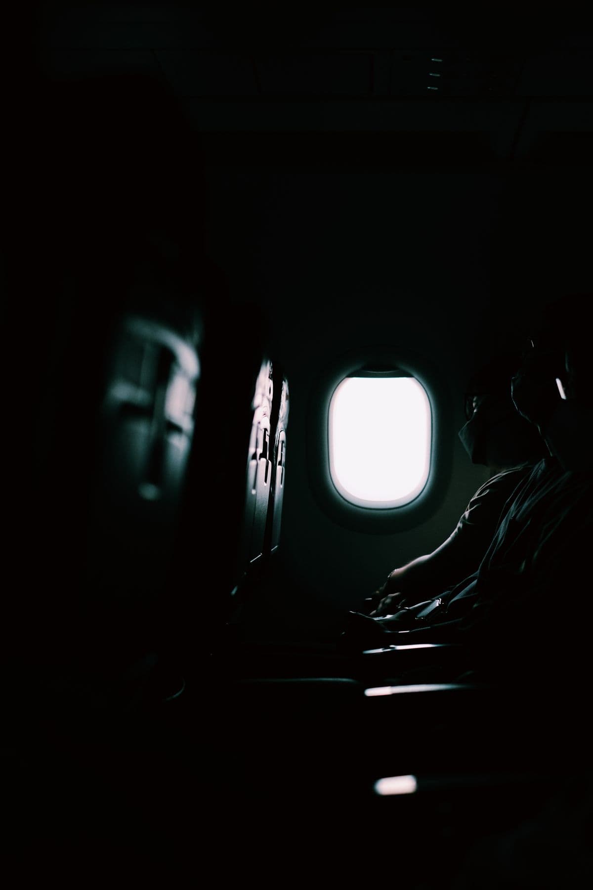A passenger silhouetted against a bright cabin window in a darkened aircraft