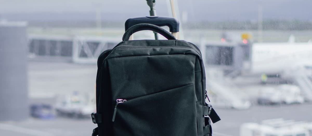 A black laptop backpack propped at a departure gate window, with jet bridges and an aircraft outside