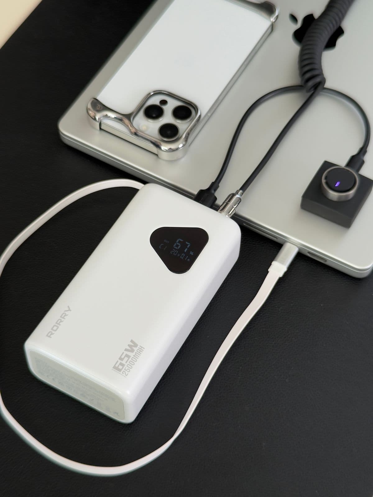 A portable power bank charging a phone and a laptop on a desk