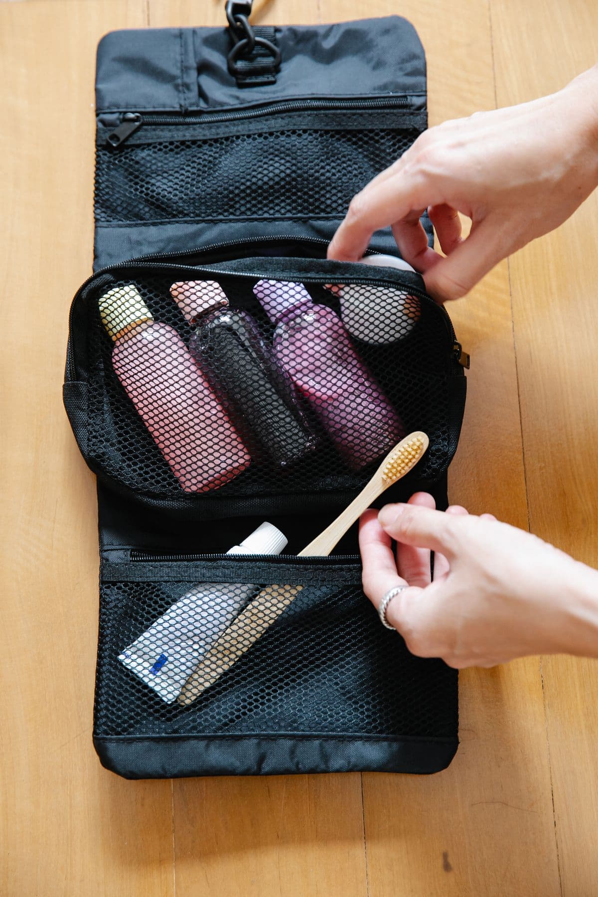 An open hanging toiletry bag with travel-sized bottles in mesh pockets